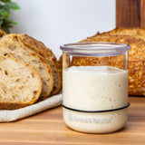 Full small sourdough Starter Jar in front of slices and a loaf of sourdough bread.